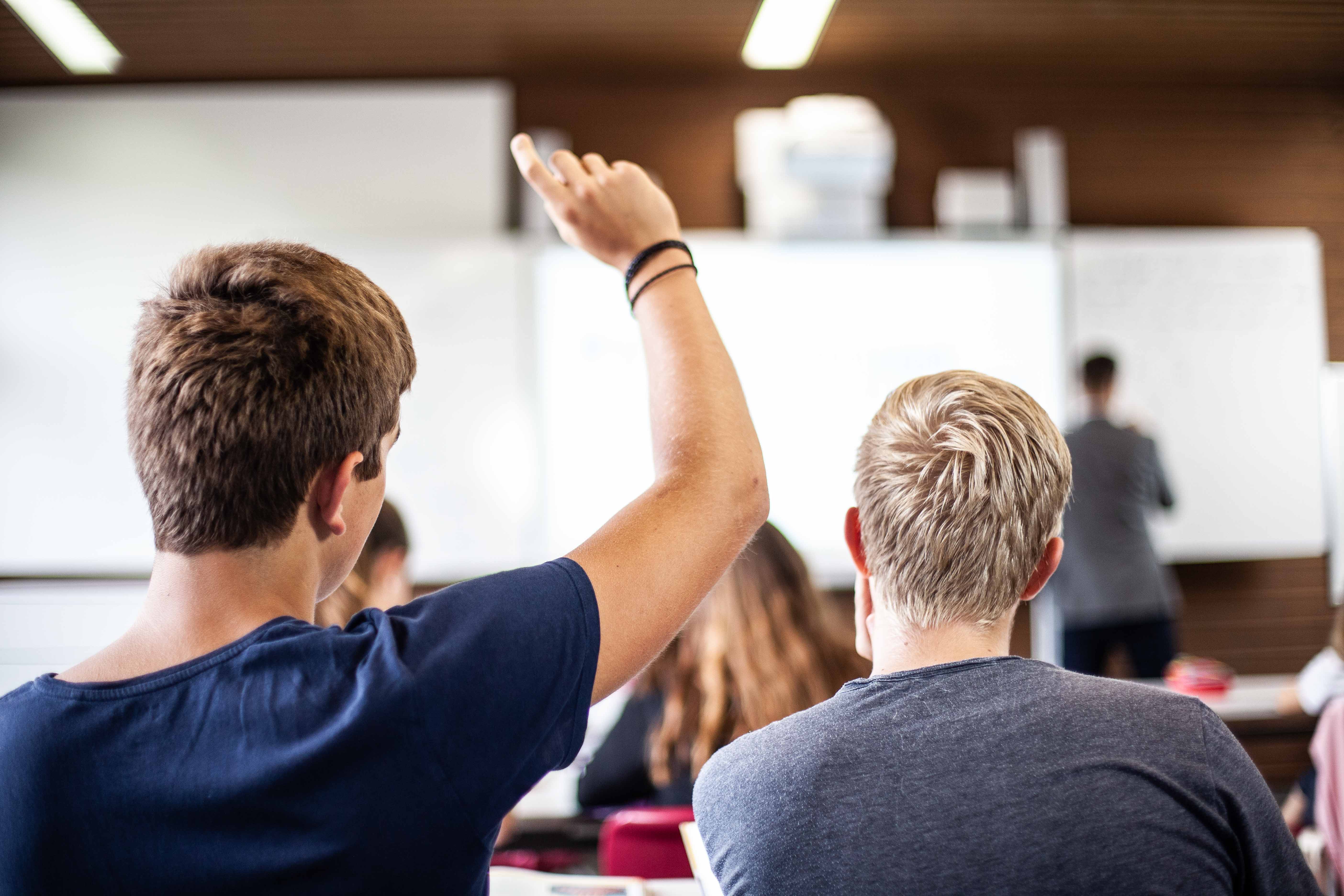 Blick zur Tafel: Schüler hat eine Wortmeldung während dem Unterricht